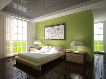 a hardwood floor, bright windows on two sides, and a two-person bed with a bedside table and lamp on each side